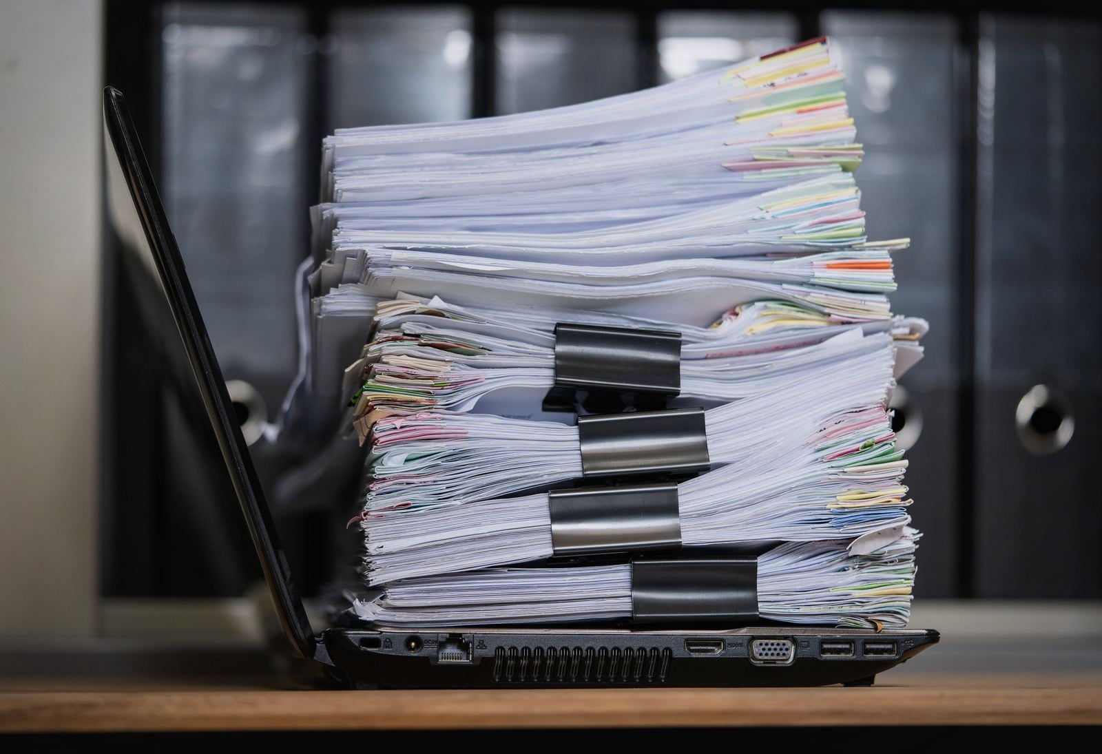 A clipped stack of paper invoices and files on a laptop, the manual accounts payable work