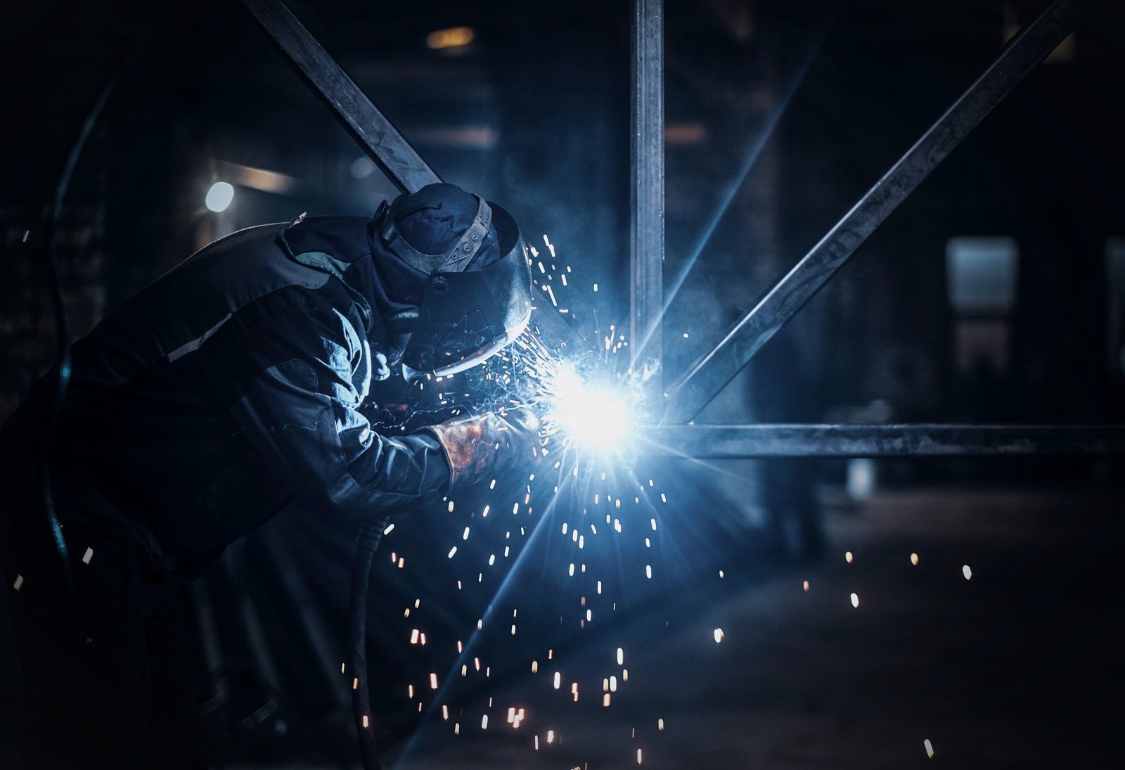 A welder at work on a steel assembly in a busy fabrication shop